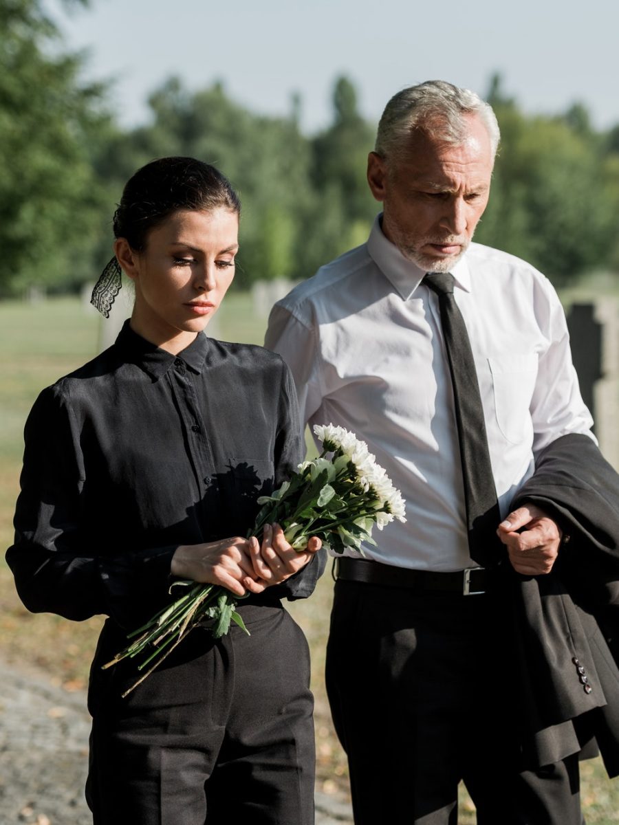 bearded-senior-man-walking-near-woman-with-flowers-on-funeral.jpg